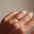 Close-up of a hand wearing a hammered gold ring with a textured finish, showcased against a neutral background. The minimalist design highlights timeless elegance and versatility.