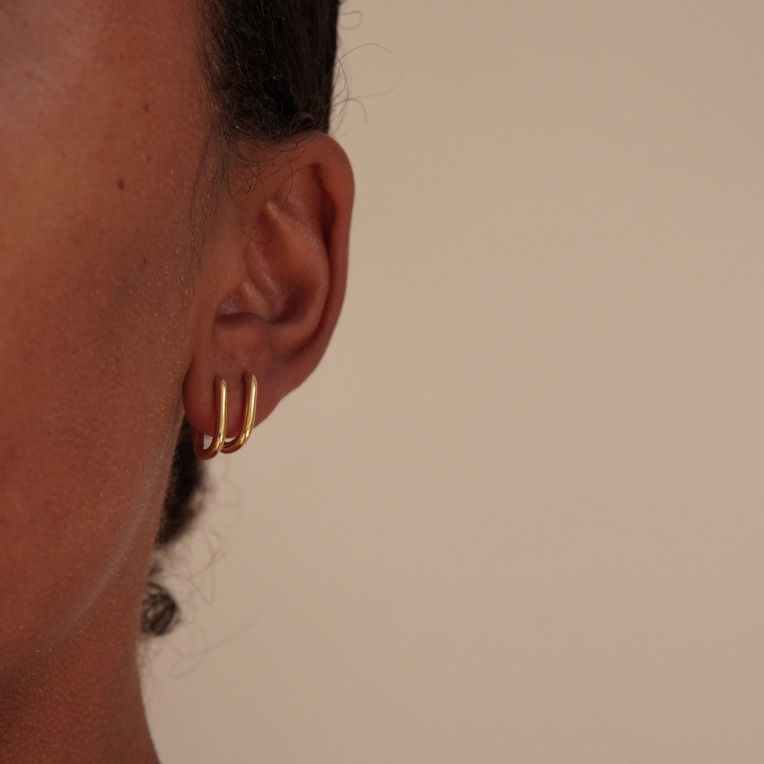 Twice our oval gold hoop earrings in an ear