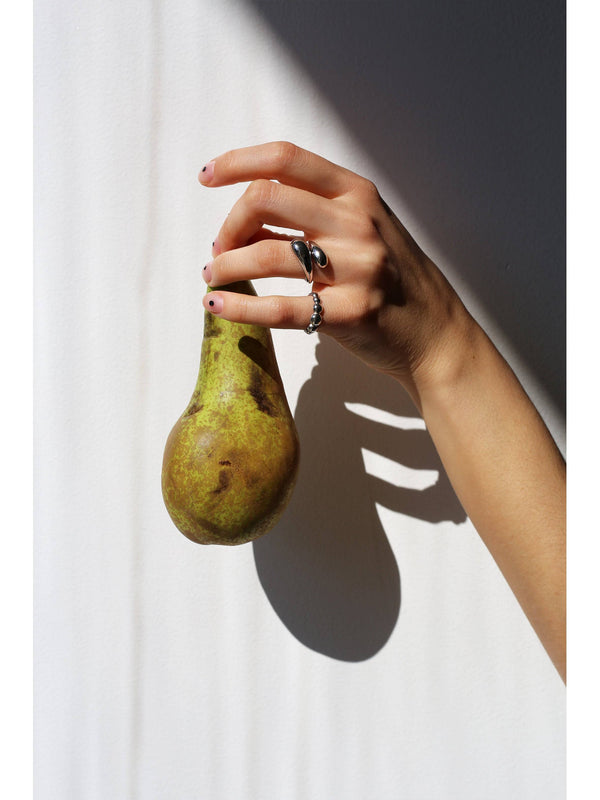 A hand filled with silver rings holding a pear