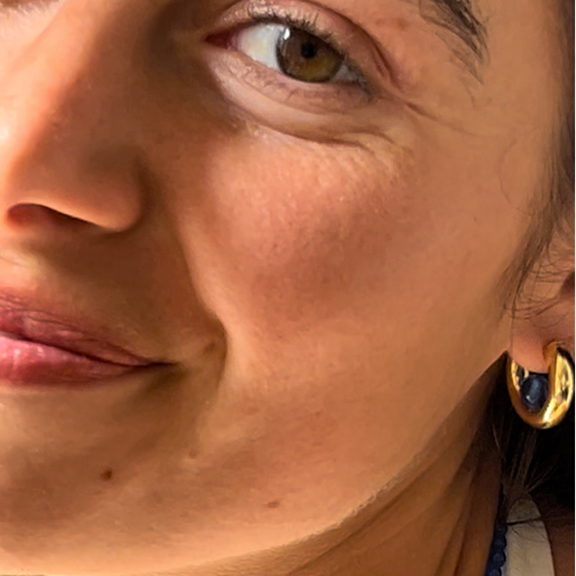 person wearing a gold hoop earring with a blue quartz gemstone in the center