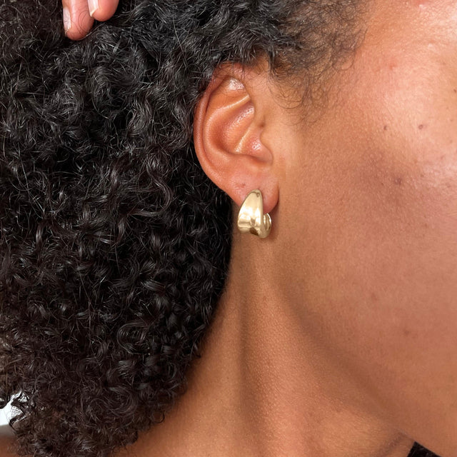 Close-up of a gold hoop earring on a model, highlighting its chunky and polished design. Perfect for adding a bold accent to any look.