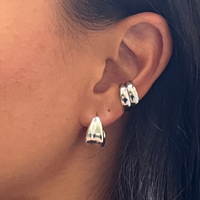 Close-up of a woman's ear wearing two silver hoop earrings, featuring a sleek and polished design. Perfect for adding a modern and sophisticated touch.