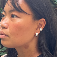 Close-up of a woman's ear wearing two silver hoop earrings, featuring a sleek and polished design. Perfect for adding a modern and sophisticated touch.