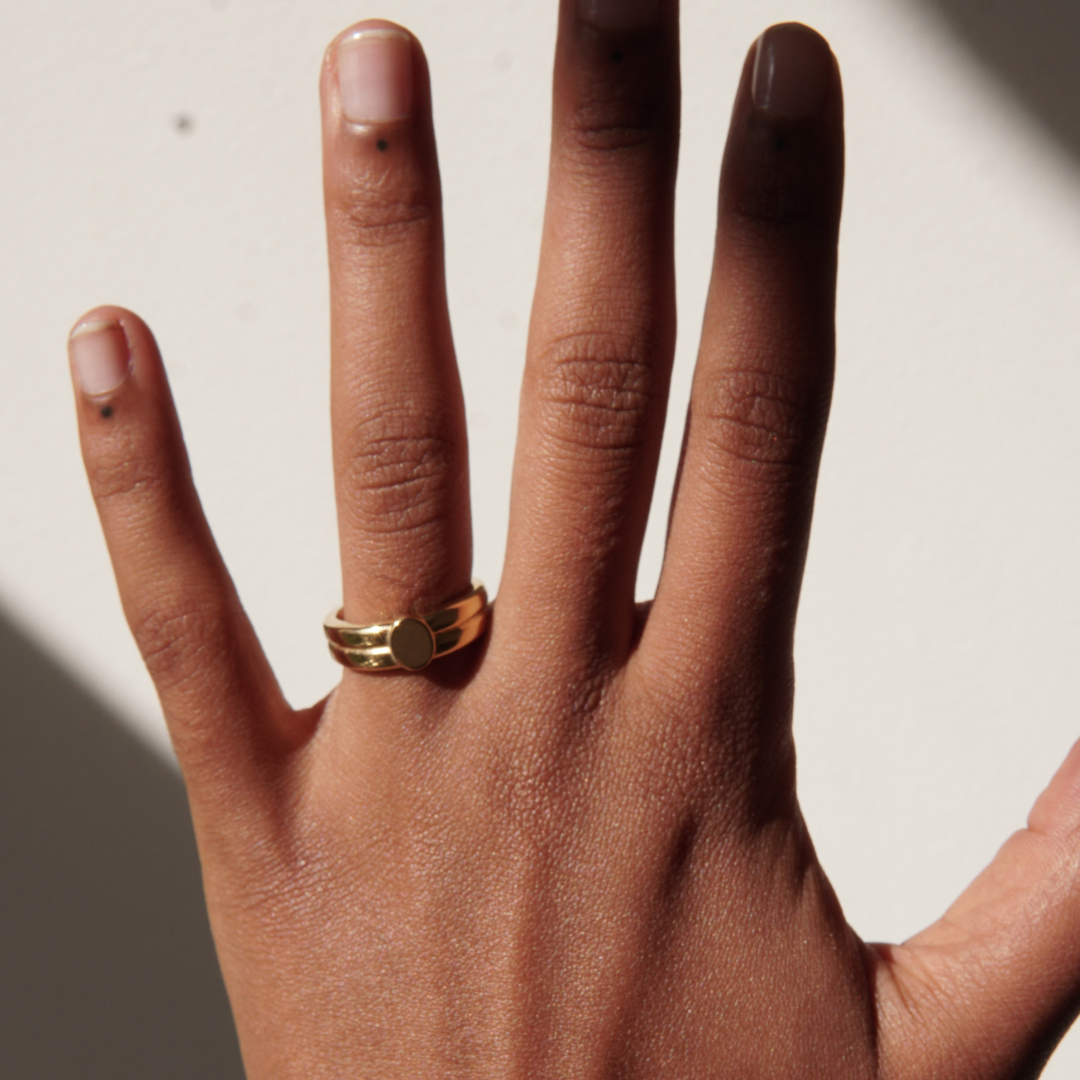 Double signet gold ring on a brown hand with dots on nails