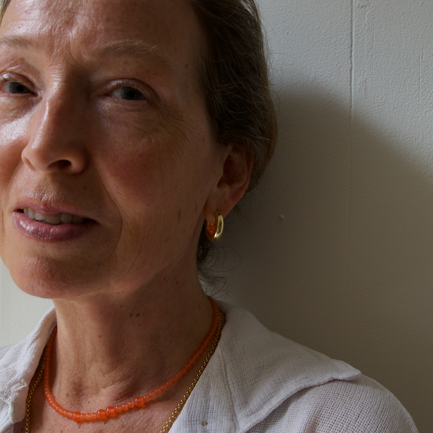 Blond lady wearing a hoop earring with a orange tangerine gemstone inside, a same gemstone necklace and a gold rolo necklace.