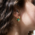 Person with curly hair earing a gold hoop earring with a green quartz gemstone inside