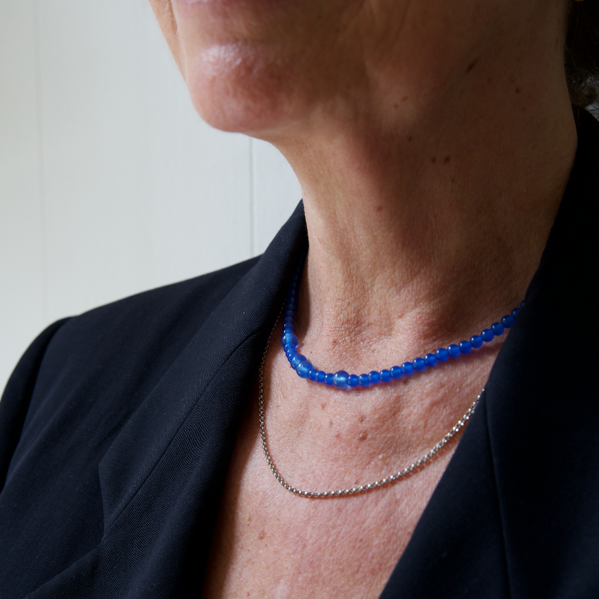 Person wearing a black blazer, a blue quartz gemstone necklace and a silver rolo chain necklace