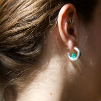 Person wearing a silver hoop earring with a green quartz gemstone in the sunlight