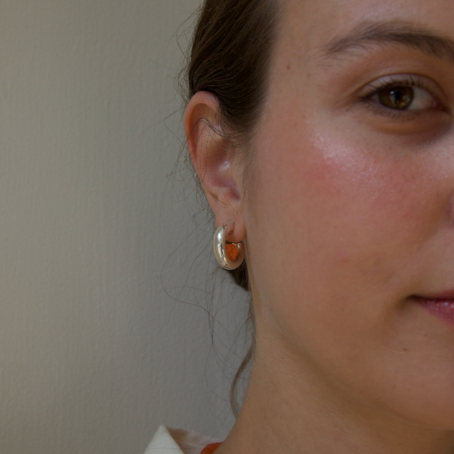 Woman with pink cheeks wearing a silver hoop with an orange tangerine gemstone inside