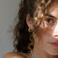 a woman with curly hair wearing a gold hoop earring with a blue lace agate gemstone. She also wears a blue lace agate gemstone necklace