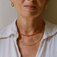 Lady in a white shirt wearing an orange tangerine gemstone necklace, a gold rolo necklace and a gold bold hoop with a tangerine quartz gemstone inside