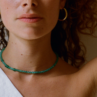 Curly hair woman wearing a green quartz gemstone necklace and a bold large hoop.