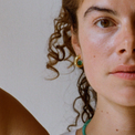 portrait of a woman with curly hair, wearing a gold hoop earring with a green quartz gemstone and a green quartz necklace