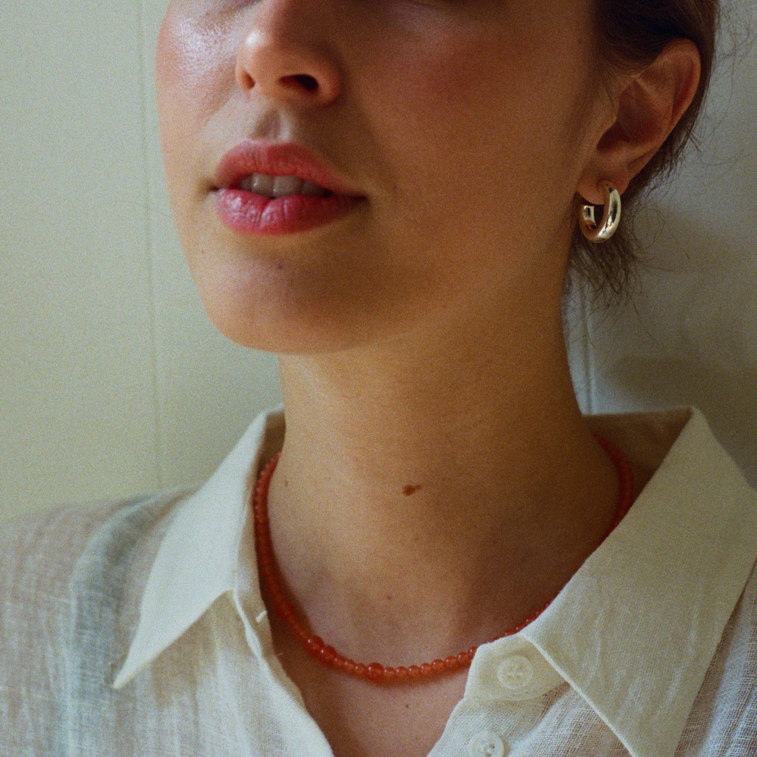 Woman in a white shirt wearing an orange tangerine gemstone necklace and a silver bold hoop