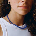 Women with curly hair wearing a white top, a blue quartz gemstone necklace and a silver bold hoop