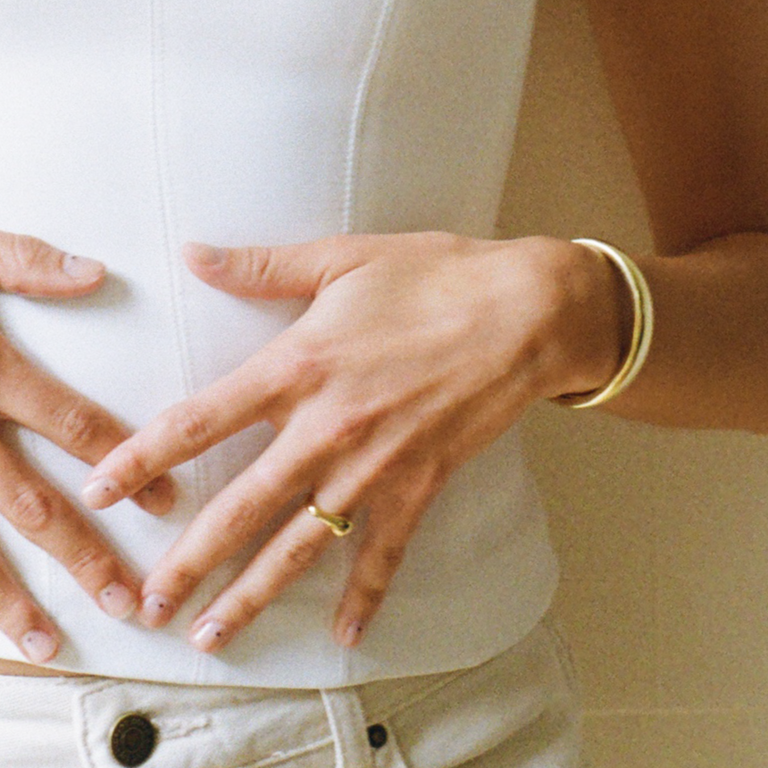 Person wearing a white shirt with a ring with uneven design on the ring finger and a cuff gold bracelet.