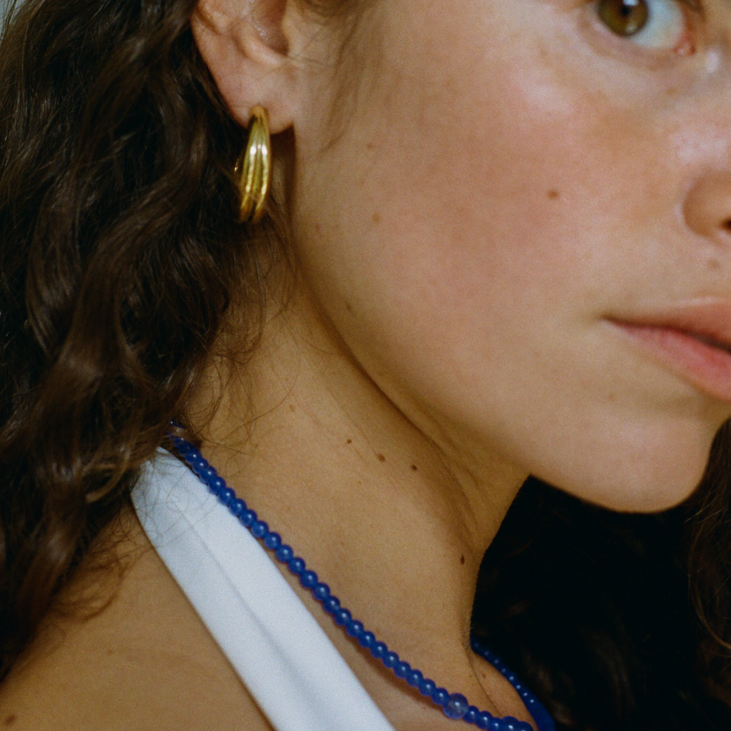 Curly hair woman looking at the camera wearing a double hoop and a blue quartz necklace