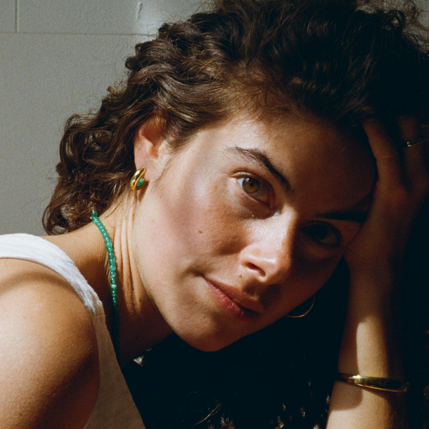 woman with curly hair, wearing a gold hoop earring with a green quartz gemstone and a green quartz gemstone necklace