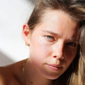 a close up of a woman with a smile on her face  enjoying the sun  with her gold jewelry blue eyes, oval earrings