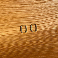 a pair of oval earrings sitting on top of a wooden table 