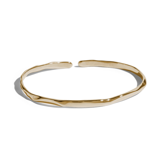 Gold cuff bracelet with a slim, uneven design, offering a minimalist and modern look. This jewelry packshot showcases the bracelet's unique texture and open-ended style