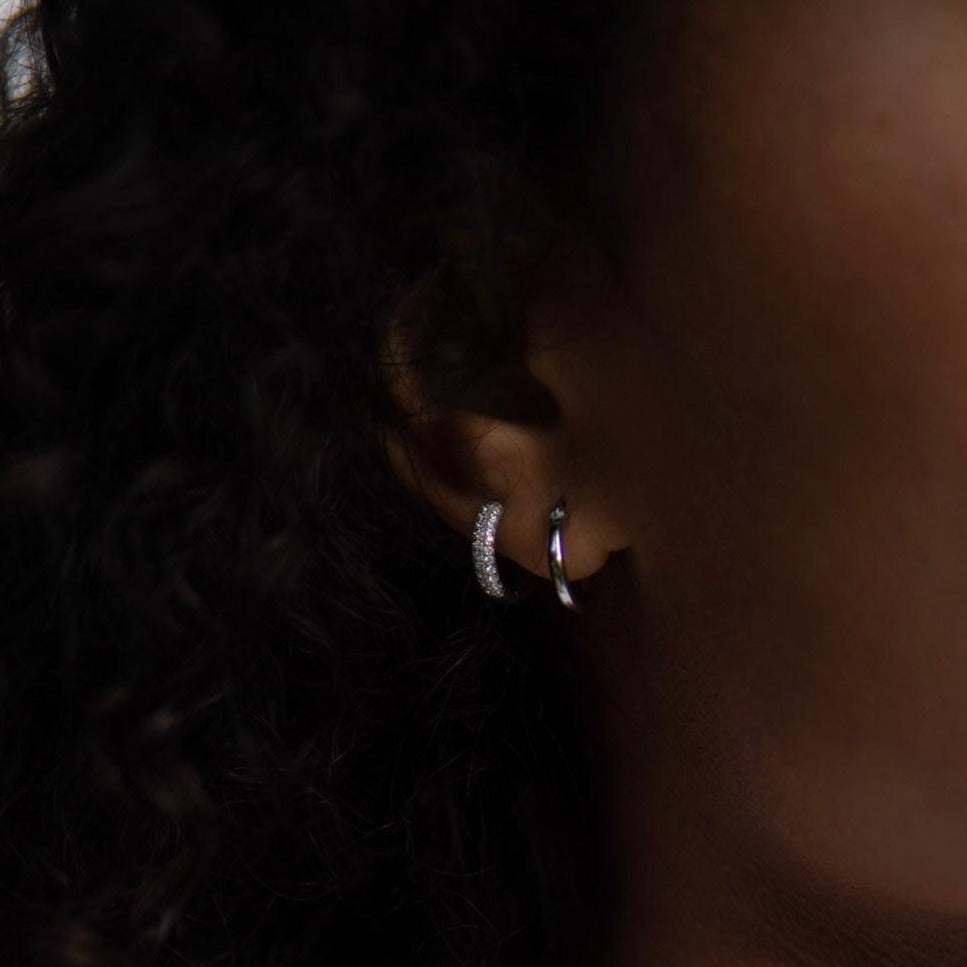 silver hoop earrings in an ear. one is minimalistic and one is a shiny hoop in silver